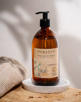 Durance Flüssigseife Neroli & Jasmin in brauner Pumpflasche auf Waschschale im Badezimmer mit Handtuch im Hintergrund