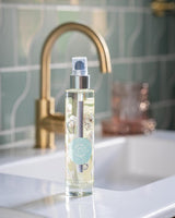 Durance Körperöl Coton Musc 100ml in transparenter Flasche auf Waschbecken im Bad mit Wasserhahn im Hintergrund