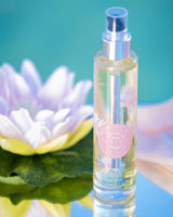 Durance Körperöl Delicate Water Lily in transparenter Flasche neben Seerose auf spiegelnder Fläche