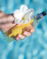 Durance Körperspray Sensual Monoi in transparenter Flasche wird in der Hand im Wasser gehalten mit Blüte