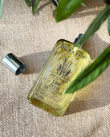 Durance Eau de Toilette L’ôme Zeste de Vétiver als Lifestyleaufnahme mit geöffnetem Flakon auf natürlichem Stoff, umgeben von grünen Blättern