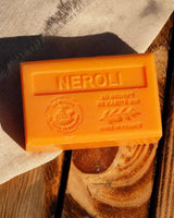 La Maison du Savon de Marseille Seife Neroli mit Bio-Sheabutter dekorativ auf einer Holzoberfläche mit natürlichem Stoff arrangiert.