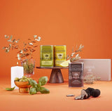 Geschenkset von A L'Olivier mit aromatisierten Olivenölen – Trüffelöl, Zitronenöl aus Nizza und Kräuteröl dekorativ arrangiert auf orangefarbenem Hintergrund, ideal als Feinkost-Geschenk für Gourmets und Liebhaber mediterraner Küche