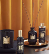 Collines de Provence Duftkollektion mit Duftkerze Schwarze Rose, Raumspray Ebenholz, Duftdiffuser Ebenholz und Duftdiffuser-Nachfüllung Ebenholz auf goldenem Tablett vor goldfarbenem Vorhang.