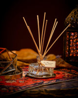 Durance Raumdiffusor Oud Mystique in Glasflakon mit Rattanstäbchen auf einem Teppich