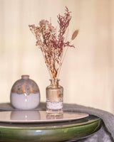Durance Floral Reed Diffuser Fleur de Coton dekorativer Raumduft mit Trockenblumen auf Tisch neben Keramikvase
