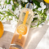 Durance Körperspray Orange Blossom in transparenter Flasche mit Blüten und Orange in sonniger Szene