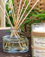 Durance Raumduft Diffuser mit Duftstäbchen neben Verbene-Duftkerze und Nachfüllflasche in natürlicher Outdoor-Dekoration
