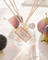 Durance Raumduft Diffuser Feigenmilch 100ml mit Duftstäbchen und dekorativem Glasflakon zwischen frischen Feigen im sonnigen Ambiente