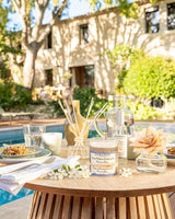Durance Raumduft Riviera Azur mit Duftkerze, Raumspray und Diffuser auf stilvoll gedecktem Gartentisch am Pool mit weißen Blüten und sommerlicher Outdoor-Dekoration
