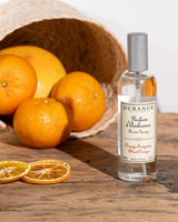 Durance Raumspray Blood Orange neben frischen Orangen und getrockneten Scheiben vor einem geflochtenen Korb