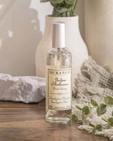Durance Raumspray Eucalyptus Minze auf Holztisch mit Vase, Stoff und Eukalyptuszweigen im Hintergrund