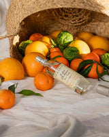 Durance Raumspray Mandarine-Bergamotte liegend vor Korb mit Orangen, Mandarinen und grünen Zitrusfrüchten in natürlicher Umgebung