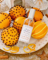 Durance Raumspray Orange-Zimt auf Teller mit Nelkenorangen, Orangenschalen und Zimtstangen in weihnachtlicher Dekoration