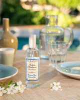 Durance Raumspray Riviera Azur auf gedecktem Tisch im Garten mit Geschirr, Glas und Blüten im sommerlichen Ambiente