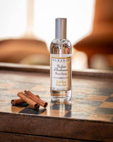 Durance Raumspray Golden Teak auf dekorativem Holztisch im Wohnzimmer mit Zimtstangen für warme holzige Raumduft Atmosphäre