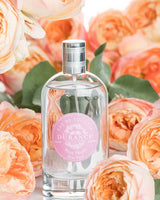 Durance Eau de Toilette Rose Pétale in stimmungsvoller Lifestyleaufnahme, umgeben von blühenden Rosen in warmen Rosé- und Apricottönen