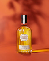 Château d'Estoublon Olivenöl Béruguette 500ml in geriffelter Glasflasche, frontal vor warmem rotem Hintergrund mit Lichtreflexen