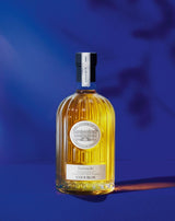 Château d'Estoublon Olivenöl Koroneiki 500ml in geriffelter Glasflasche, frontal vor tiefblauem Hintergrund mit Licht und Schatten