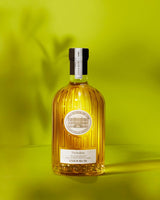 Château d'Estoublon Olivenöl Picholine 500ml in geriffelter Glasflasche, frontal vor leuchtend gelbgrünem Hintergrund mit Schatten