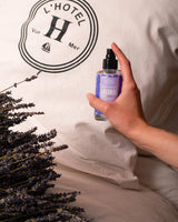 Panier des Sens Kissenspray Lavendel aus der Provence 100ml bei der Anwendung auf einem Kopfkissen mit Lavendelzweigen in entspannender Schlafzimmeratmosphäre
