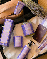 Panier des Sens Lavendel aus der Ikonischen Lavendel-Kollektion im geöffneten Reisekoffer. Zu sehen sind Duftstäbchen-Diffuser, Flüssigseife, Duftkerze, Körperlotion, Handcreme und Eau de Toilette neben Reisepass und Boardingpass.