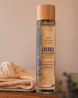 Panier des Sens Massage- und Körperöl Lavendel aus der Provence 100ml in eleganter Glasflasche mit Holzverschluss, dekorativ neben einem Handtuch arrangiert.